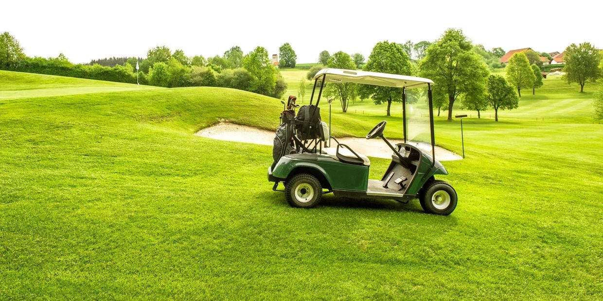 Golf cart parked on a green golf course.