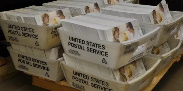 Stacks of United States Postal Service mail tubs filled with letters.