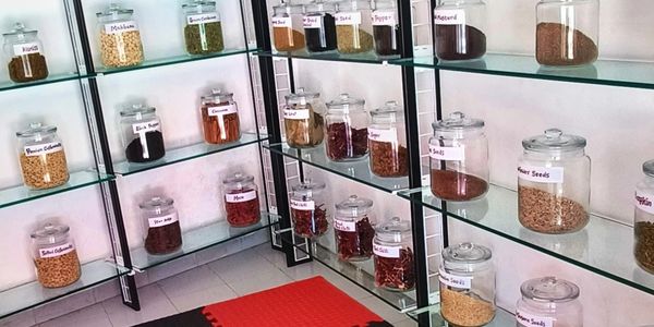 A neatly arranged spice and nut storage area with labeled jars on glass shelves.