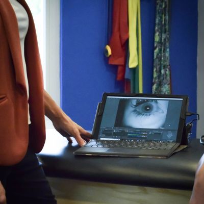 Person standing next to a tablet displaying an eye close-up.
