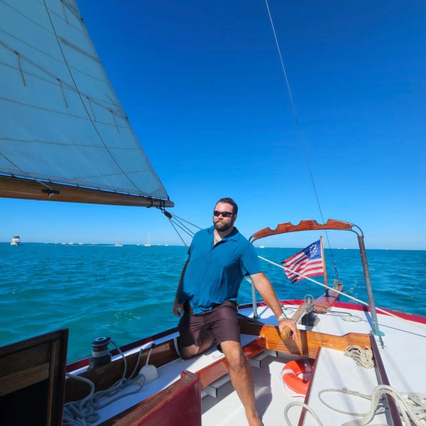 Man relaxing on a sailboat under clear blue skies.