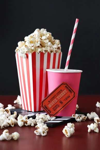 Popcorn in a red-striped box with a drink and movie ticket on a dark background.