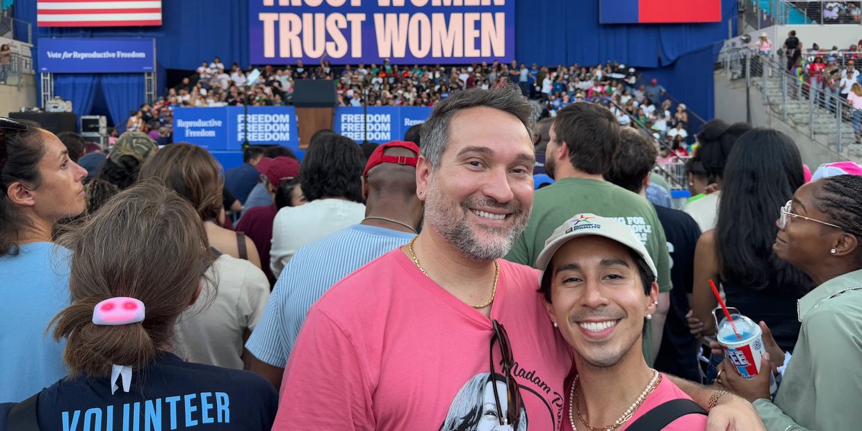 Two smiling men in pink shirts at a crowded women's rights rally.
