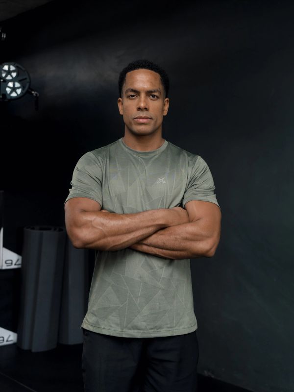 Confident man with crossed arms in gym attire against dark background.