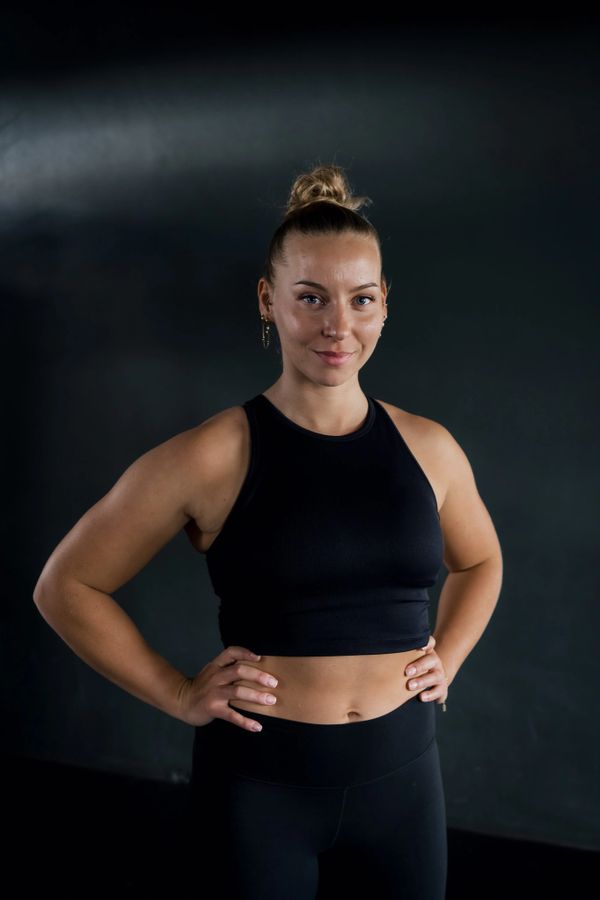 Fit woman in black workout clothes poses confidently with hands on hips.