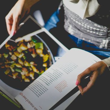 Person reading a cookbook with a colorful dish nearby.
