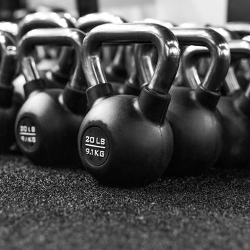 Black kettlebells lined up on a gym floor.