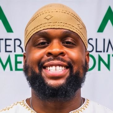 Smiling man wearing a beige cap and traditional attire.
