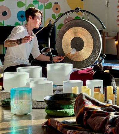 Person playing a gong surrounded by crystal singing bowls and candles.