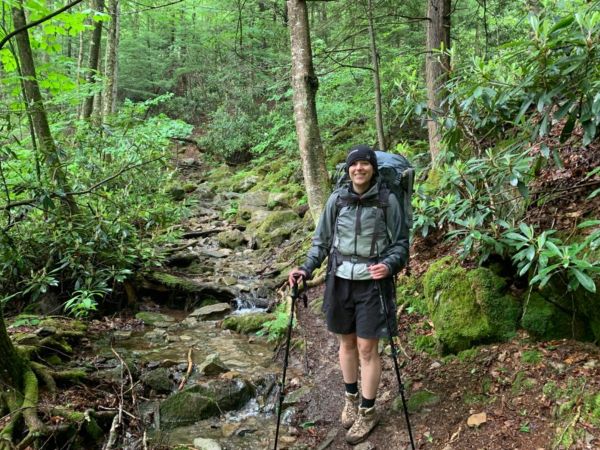 Smiling hiker with trekking poles on a lush forest trail.