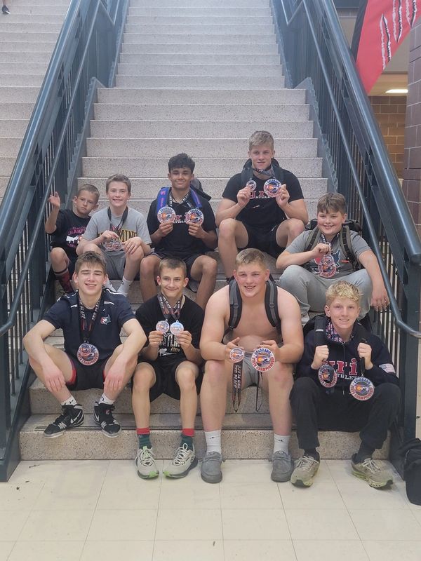 A group of boys proudly displaying their medals while sitting on stairs.