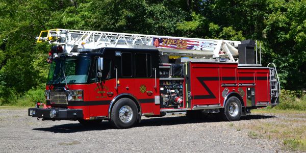 Red fire truck with extended ladder on a gravel road.