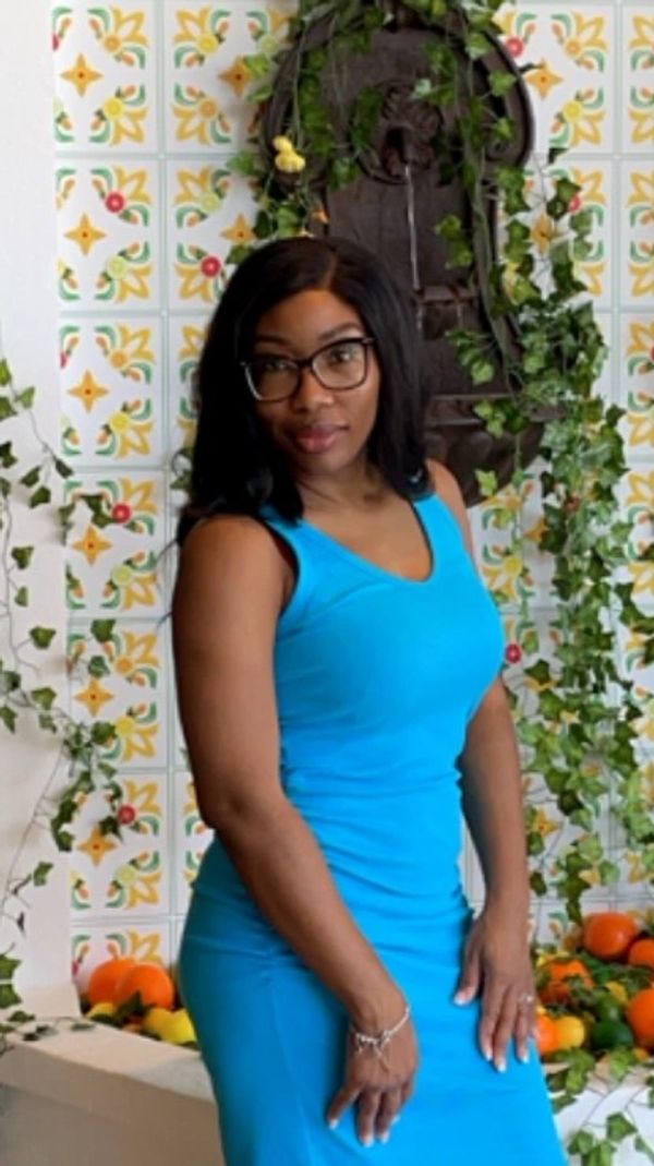 Woman in blue dress posing by a colorful floral wall.