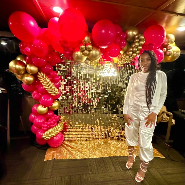 Woman standing in front of red and gold balloon decoration.