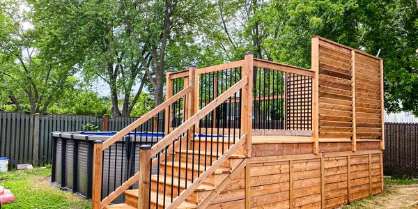 Wooden deck with stairs surrounding an above-ground pool in a backyard.