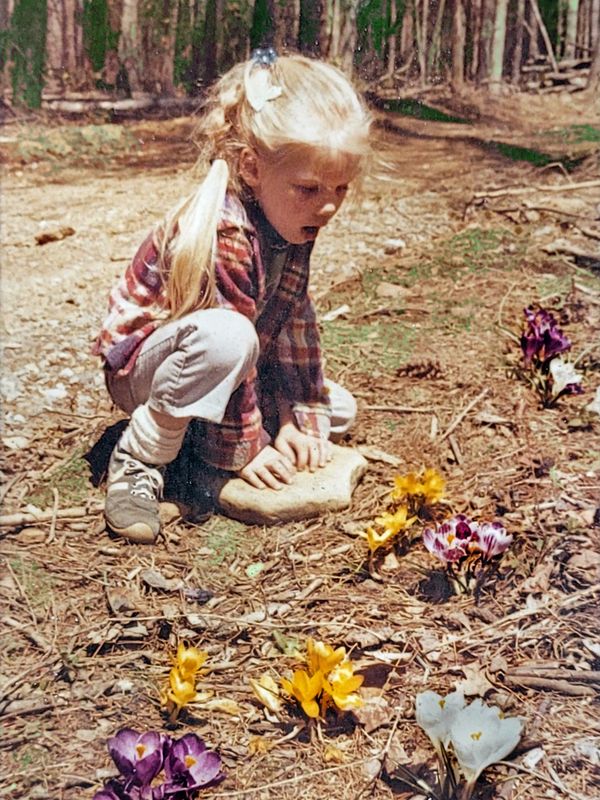 Kelsey as a little girl.  She is looking with delight at some wild flowers on the forest floor.