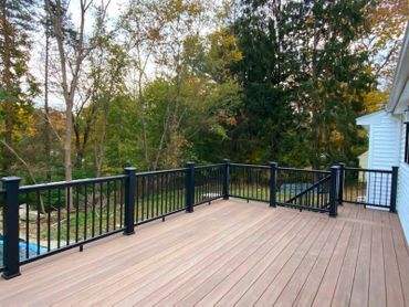 Spacious wooden deck with black metal railing overlooking a green, wooded area.