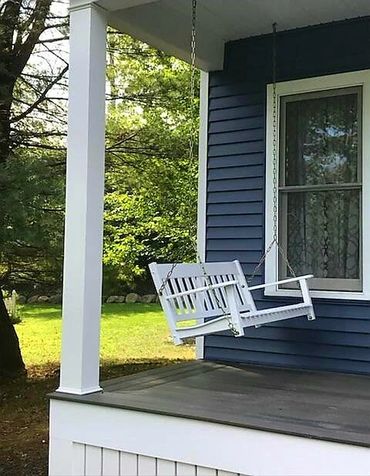 White porch swing hanging on a blue house porch in daylight.