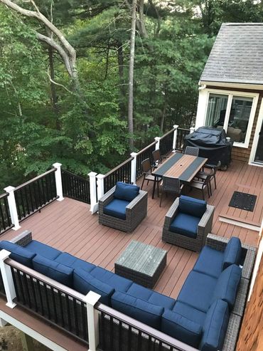 Spacious outdoor deck with blue cushioned seating and dining area surrounded by trees.