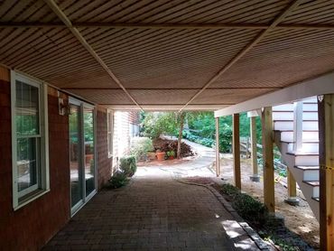 Covered patio with brick flooring and wooden ceiling, leading to a garden path.