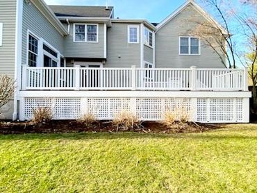 A white wooden deck attached to a beige house with a green lawn.