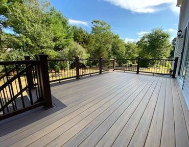 Spacious outdoor deck with wooden railings and lush green trees in the background.