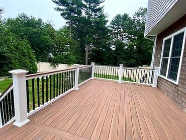 Spacious wooden deck attached to a house with a black and white railing.