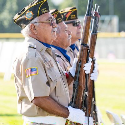 alt="Veteran firing party performing three-volley salute at a funeral"