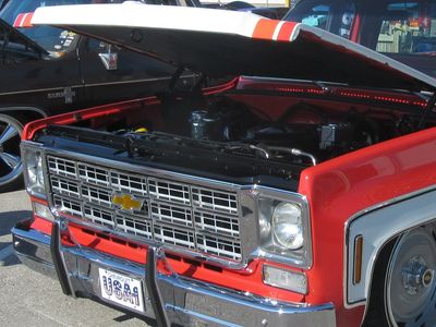 A red and white 1975 Chevrolet C10 in a parking spot with its hood opened. 