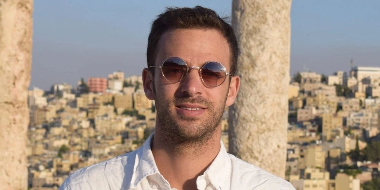 Man wearing round sunglasses and white shirt outdoors.