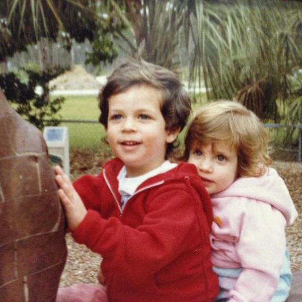 Two children playing outdoors, one in red and one in pink hoodie.