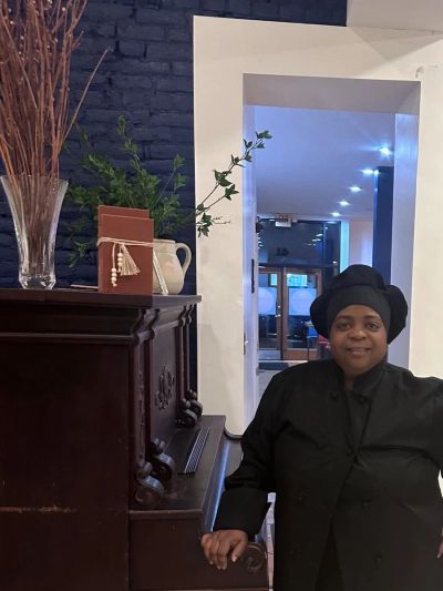 Chef in black uniform smiling indoors near piano.