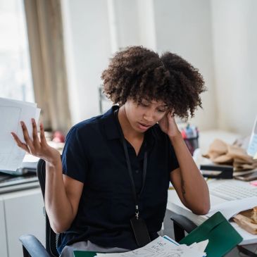 Woman looking stressed at paperwork in office.