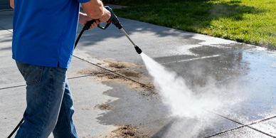 Person pressure washing a dirty concrete driveway outdoors.