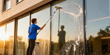 Person cleaning large glass window with a squeegee on a ladder during sunset.
