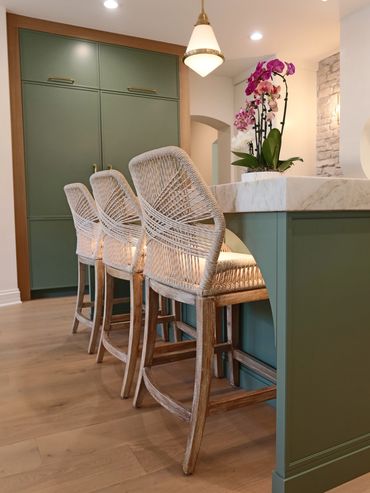 Three woven bar stools at a green kitchen island with orchid centerpiece.