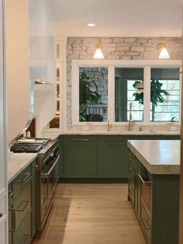 Modern kitchen with green cabinets, marble countertops, and stone wall accents.