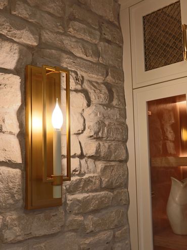 Elegant gold wall sconce illuminates a textured stone wall beside a glass cabinet.