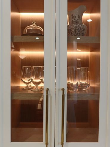 Glassware and a decorative pitcher displayed in a lit wooden cabinet with glass doors.