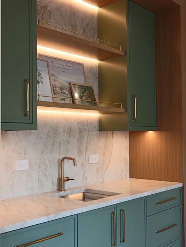 Modern kitchen with green cabinets, marble countertop, and warm lighting.