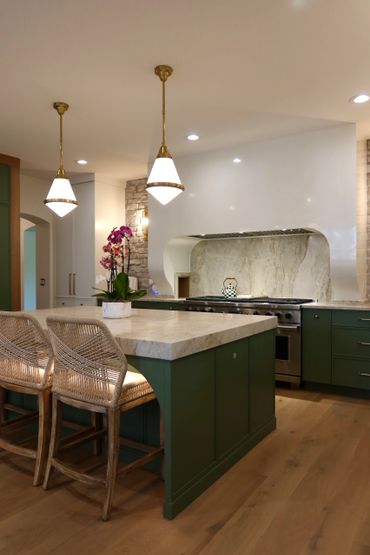 Modern kitchen with green cabinets, marble countertop, and pendant lights.