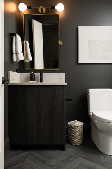 Modern bathroom with dark wood vanity, gold-framed mirror, and white toilet.