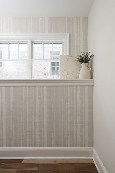 Minimalist interior with neutral wallpaper, decorative vase, and textured art piece by a window.