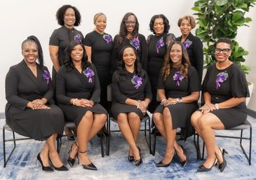 Group of women in black dresses with purple corsages posing together.