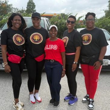 Group of five women posing outdoors, some wearing matching shirts.