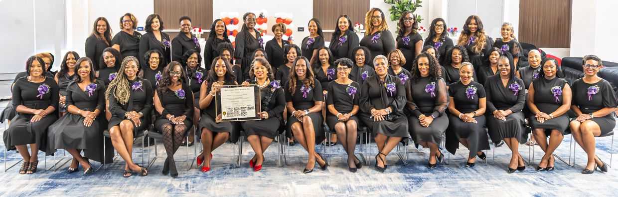 Group of women dressed in black with purple ribbons posing for a photo.