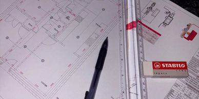 Architectural blueprints with a pen, eraser, and scale ruler on a desk.