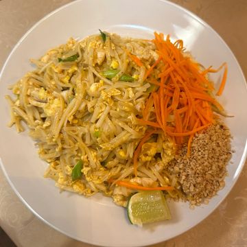 Plate of Pad Thai with bean sprouts, shredded carrots, crushed peanuts, and lime wedge.