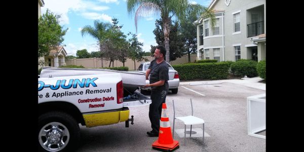 Man loading a mattress into a junk removal truck in a residential area.