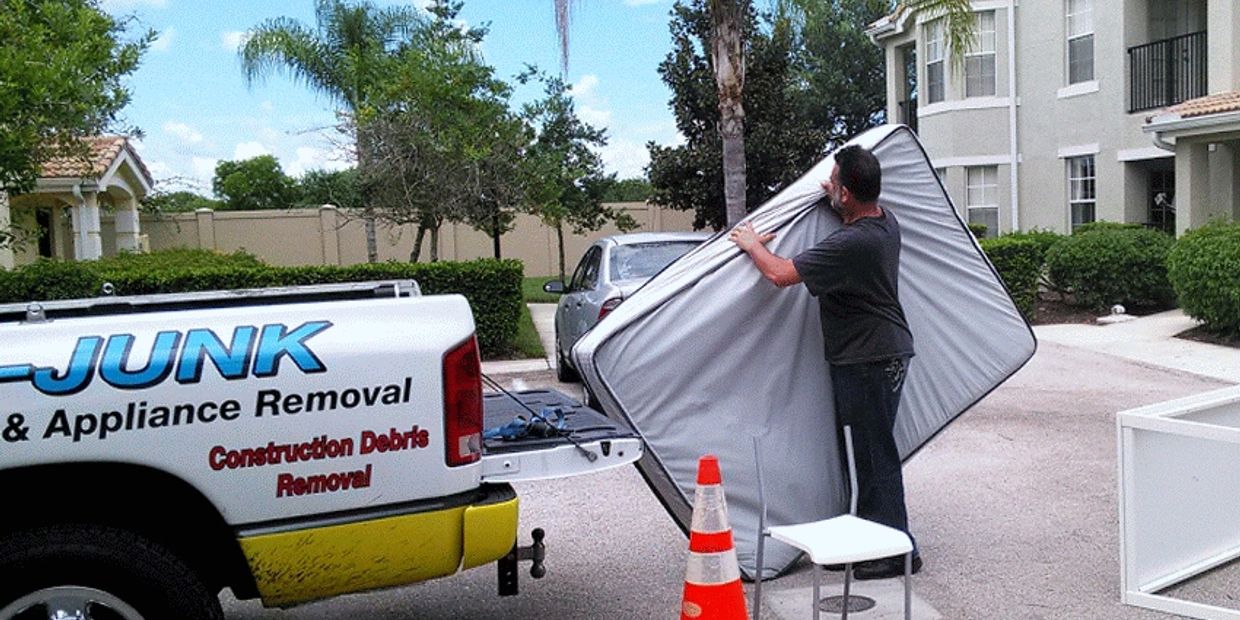 Man loading a mattress into a junk removal truck in a suburban neighborhood.